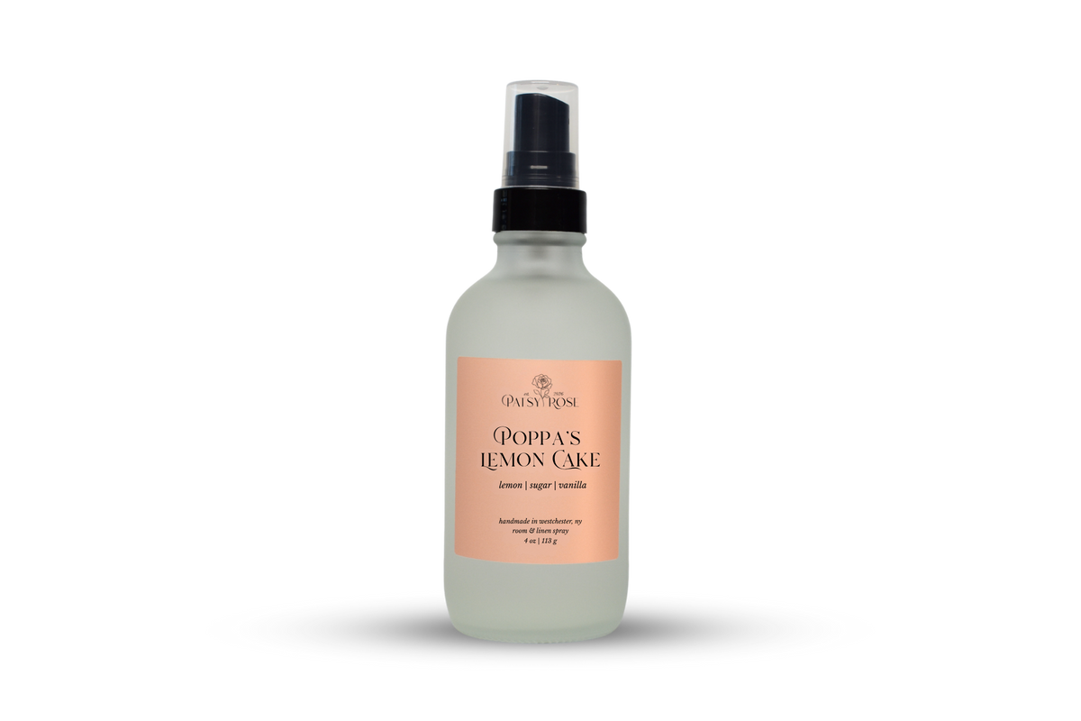 A 4 oz room and linen spray made by Patsy Rose in a frosted glass bottle with a peach label that says "Poppa's Lemon Cake" with a scent of "lemon, sugar, vanilla" on a white background.