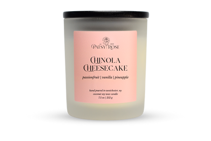 A 7.5 oz soy wax candle by Patsy Rose in the 'Chinola Cheesecake' 'passionfruit | vanilla | pineapple' scent. The candle is in a frosted glass jar with a black lid and a peach-pink label, set against a plain white background.