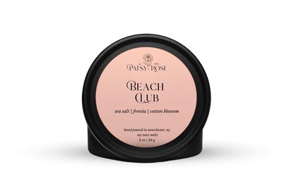 Hand-poured soy wax melts made by Patsy Rose with black tins and a peach label that says "Beach Club" with scent notes of "sea salt, freesia, cotton blossom".