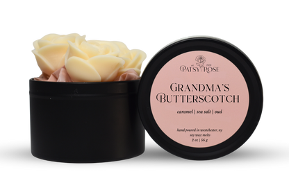 Hand-poured, rose shaped soy wax melts made by Patsy Rose with black tins and a peach label that says "Grandma's Butterscotch" with scent notes of "caramel, sea salt, oud".