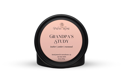 Hand-poured soy wax melts made by Patsy Rose with black tins and a peach label that says "Grandpa's Study" with scent notes of "leather, amber, rosewood".