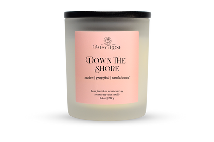 A 7.5 oz soy wax candle by Patsy Rose in the 'Down The Shore' 'melon | grapefruit | sandalwood' scent. The candle is in a frosted glass jar with a black lid and a peach-pink label, set against a plain white background.
