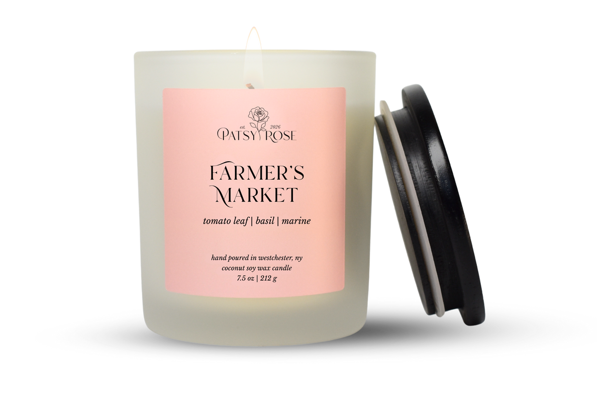A 7.5 oz single-wick candle in a frosted glass jar with a pale pink label reading 'Patsy Rose Farmer's Market' and 'tomato leaf | basil | marine.' A black lid is leaning against the right side of the jar on a clean white background.
