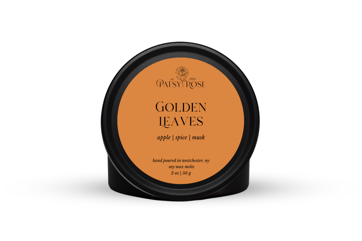 Hand-poured soy wax melts made by Patsy Rose with black tins and an orange label that says "Golden Leaves" with scent notes of "apple, spice, musk".
