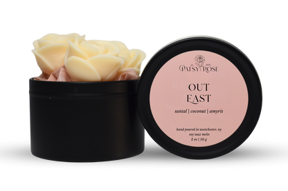 Hand-poured, rose shaped soy wax melts made by Patsy Rose with black tins and a peach label that says "Out East" with scent notes of "santal, coconut, amyris".