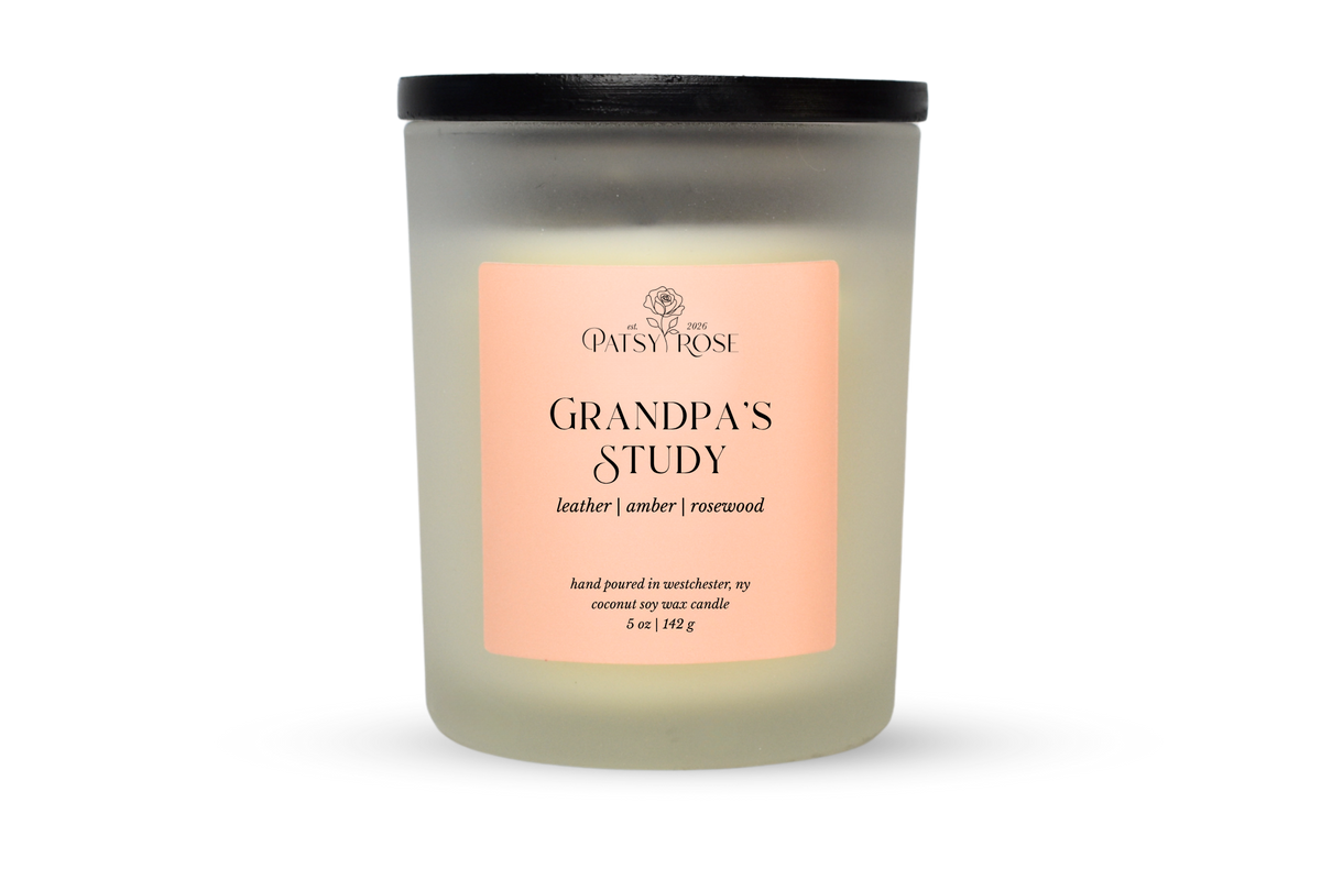 A 5 oz soy wax candle by Patsy Rose in the 'Grandpa's Study' 'leather| amber | rosewood' scent. The candle is in a frosted glass jar with a black lid and a peach-pink label, set against a plain white background.