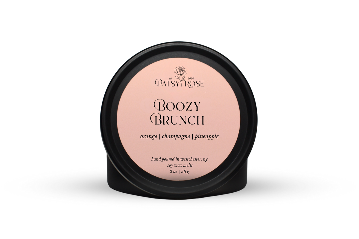 Hand-poured soy wax melts made by Patsy Rose with black tins and a peach label that says "Boozy Brunch" with scent notes of "orange, champagne, pineapple".