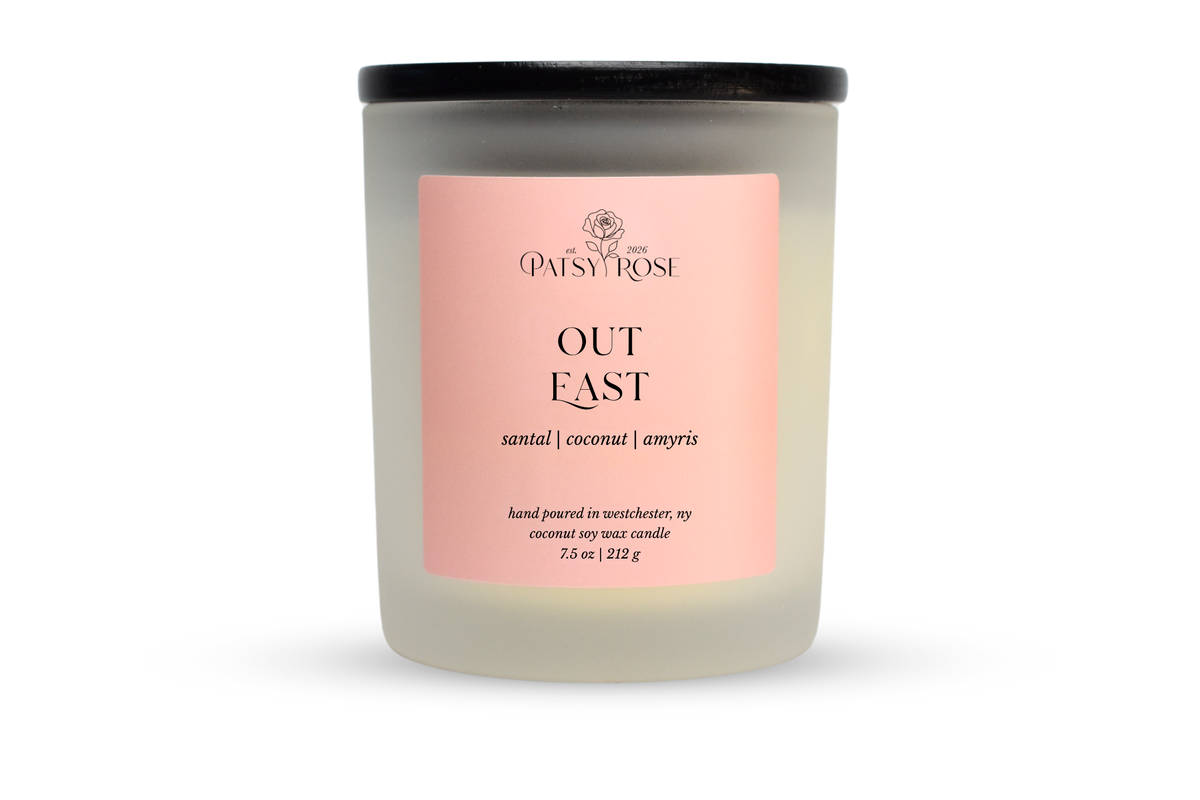A 7.5 oz soy wax candle by Patsy Rose in the 'Out East' 'santal | coconut | amyris' scent. The candle is in a frosted glass jar with a black lid and a peach-pink label, set against a plain white background.