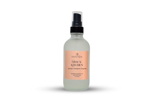 A 4 oz room and linen spray made by Patsy Rose in a frosted glass bottle with a peach label that says "Doc's Kitchen" with a scent of "lavender, lemongrass, bergamot" on a white background