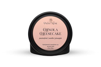 Hand-poured soy wax melts made by Patsy Rose with black tins and a peach label that says "Chinola Cheesecake" with scent notes of "passionfruit, vanilla, pineapple".