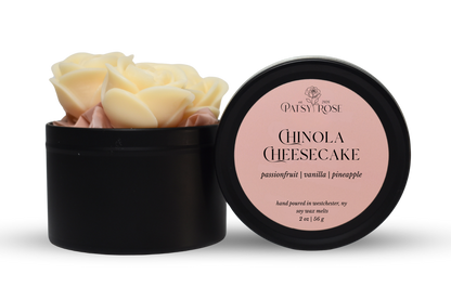 Hand-poured, rose shaped soy wax melts made by Patsy Rose with black tins and a peach label that says "Chinola Cheesecake" with scent notes of "passionfruit, vanilla, pineapple".